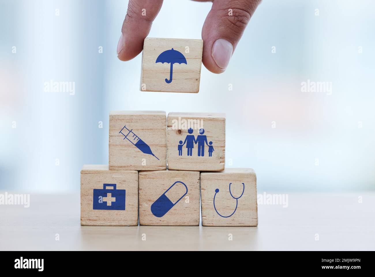 Hands, wood and building blocks on table for insurance, healthcare or a safe healthy foundation. Hand of doctor putting small wooden block, object or Stock Photo
