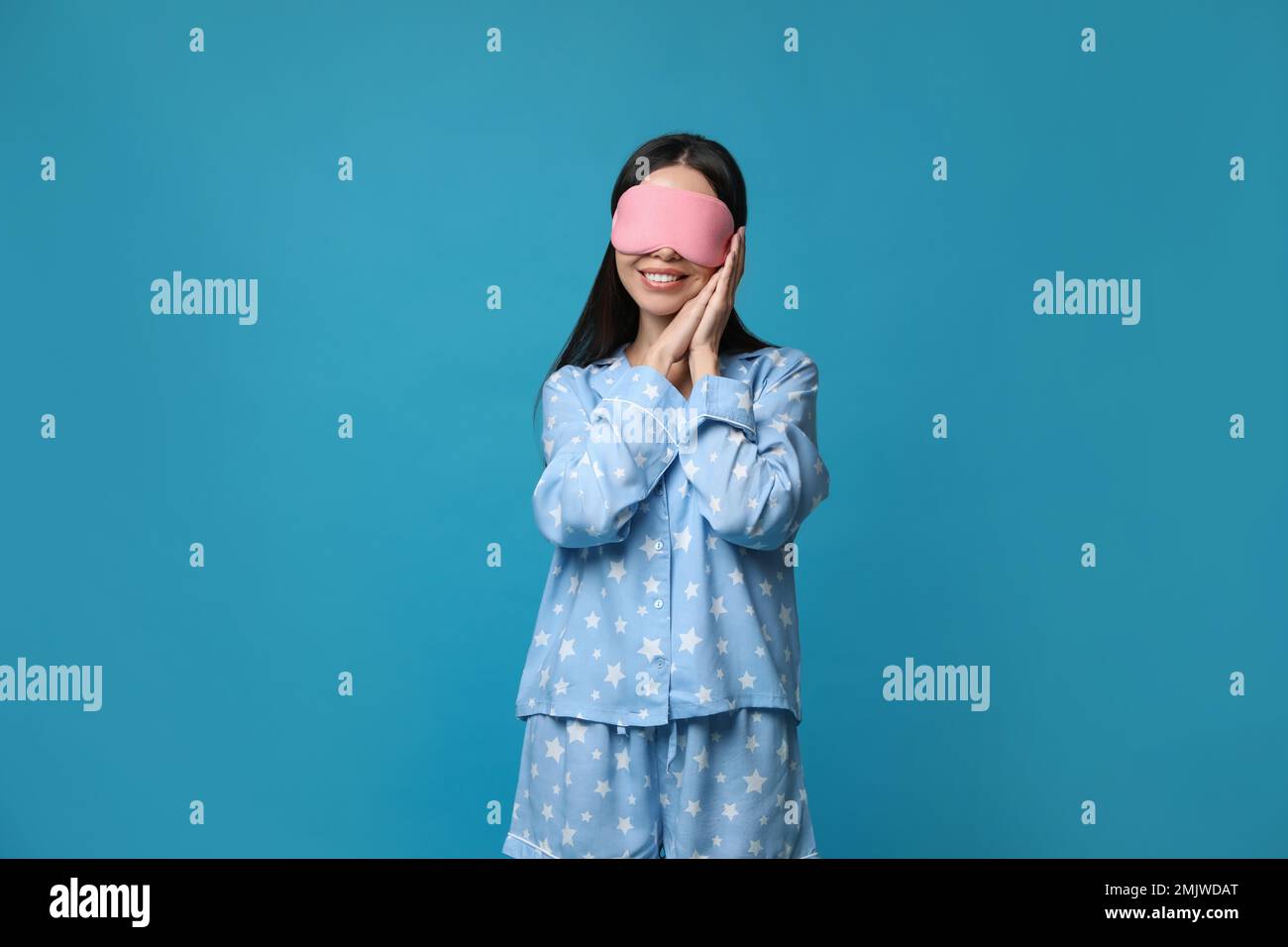 Young woman wearing pajamas and sleeping mask on blue background. Bedtime Stock Photo