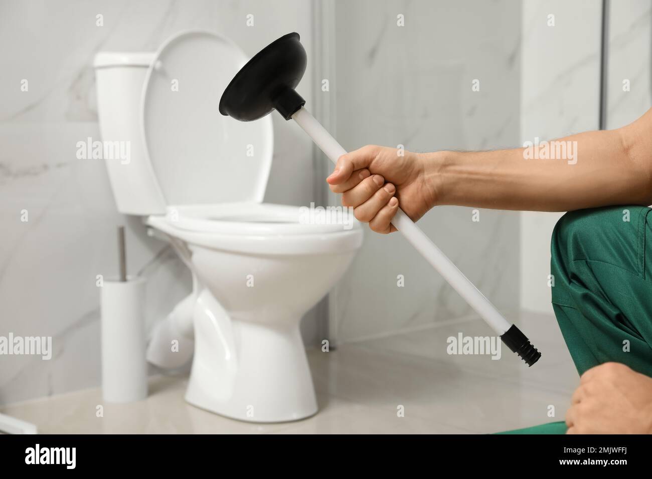 Professional plumber holding plunger near toilet bowl in bathroom