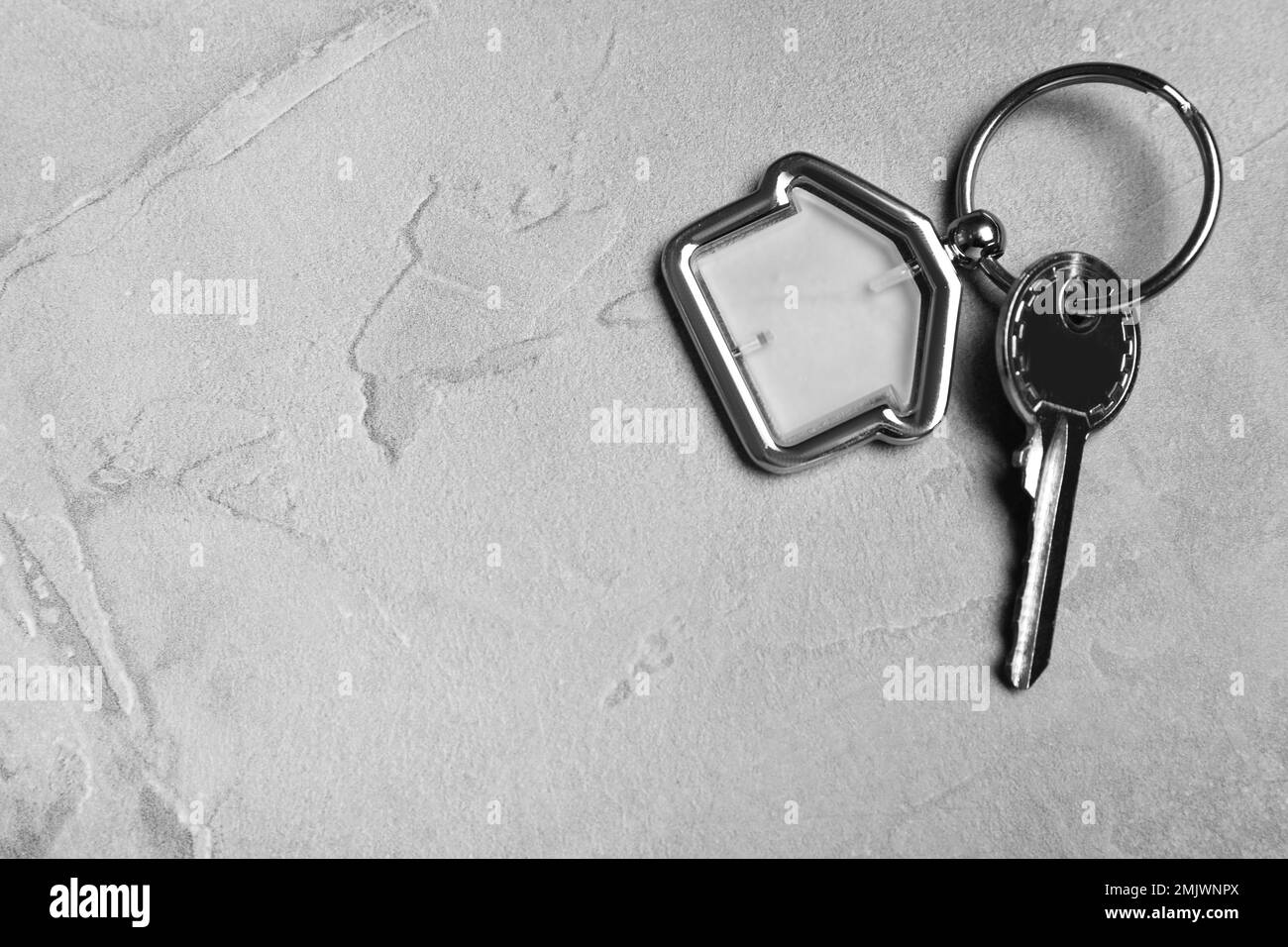 Key with trinket in shape of house on grey stone background, top view and space for text. Real estate agent services Stock Photo