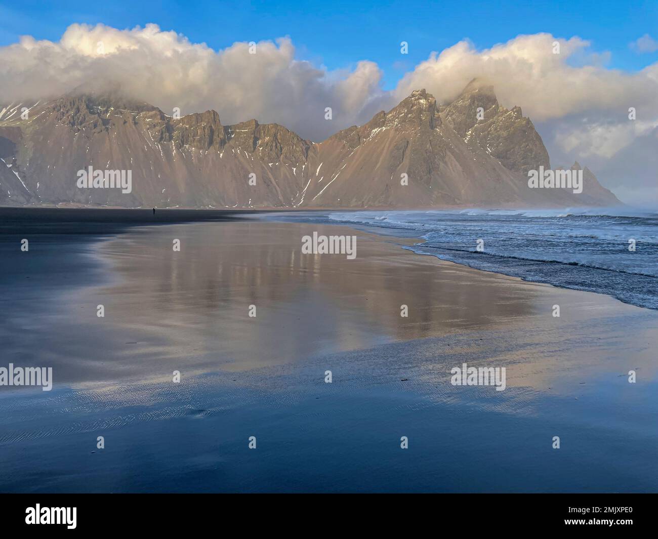 Mountains by the sea with reflections in sand Stock Photo