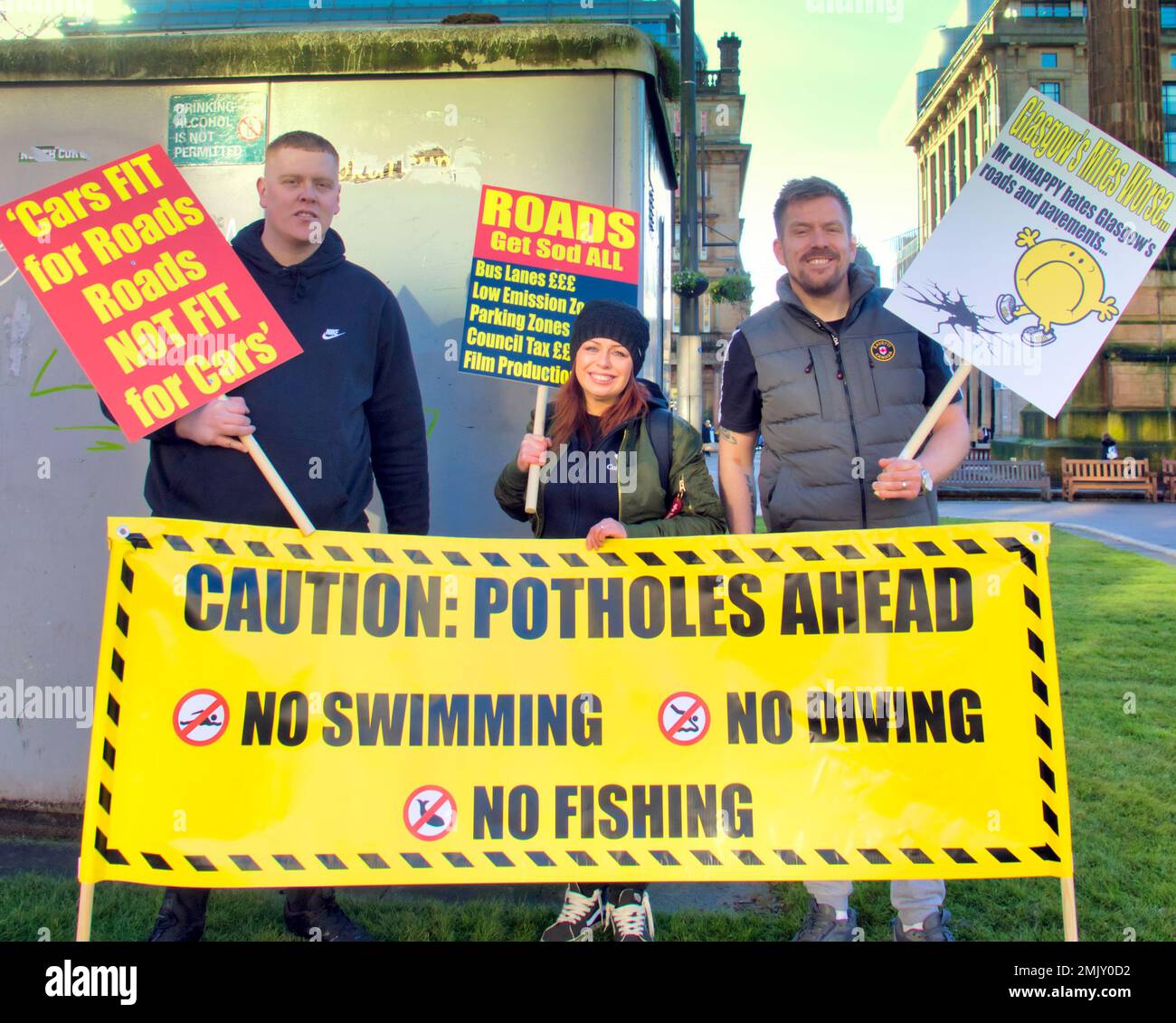 Glasgow, Scotland, UK 28th  January, 2023. Pothole protest outside council headquarters in george square saw a large crowd of placard waving demonstrators with a crowd funded banner gain the approval of passing motorists as they posed by the side of the road with a a large pothole. Credit  Gerard Ferry/Alamy Live News Stock Photo