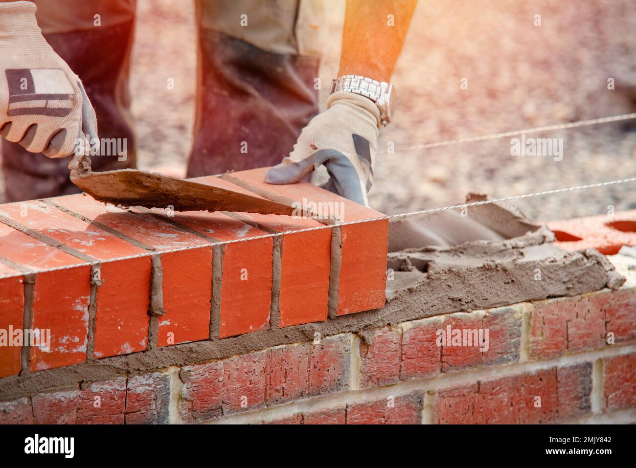Industrial bricklayer laying bricks on cement mix on construction site