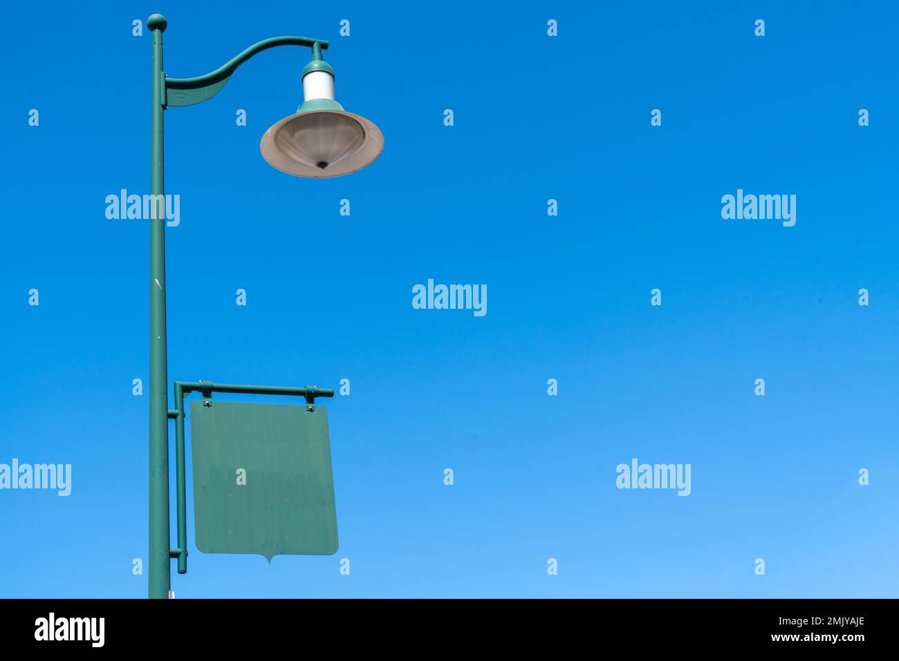real old vintage green lamp post with an empty sign banner in blue sky