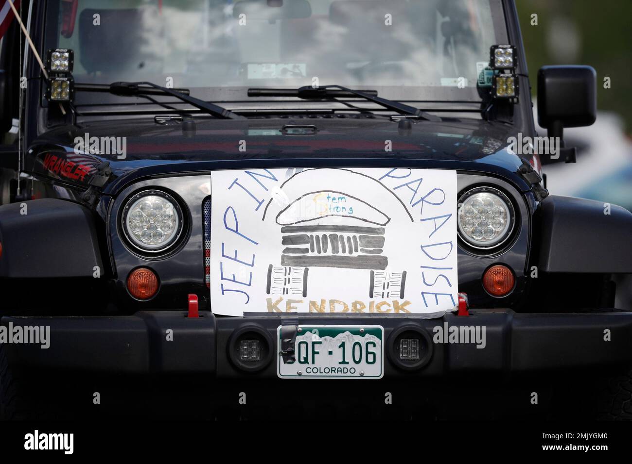 A sign is placed in front of the grille of a Jeep Wrangler while parked