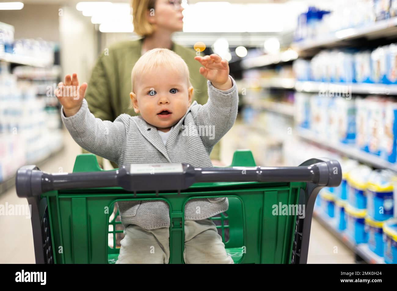 Mother pushing shopping cart with her infant baby boy child down