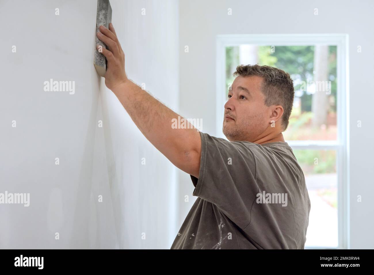 Worker sanding drywall mud in room during renovation of house with use sand trowel Stock Photo