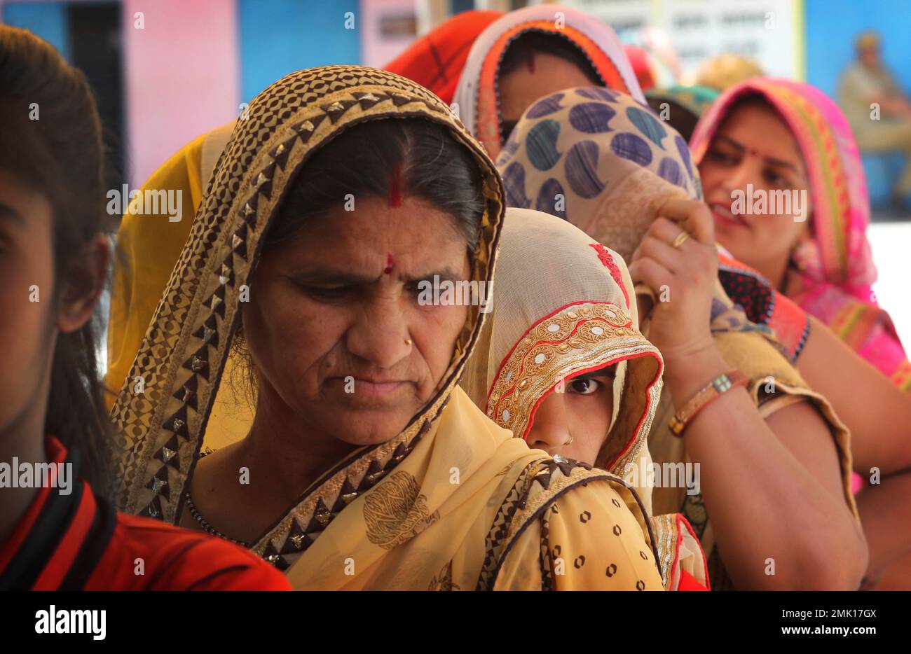 Indian women stand in a queue to cast their vote at a polling station ...