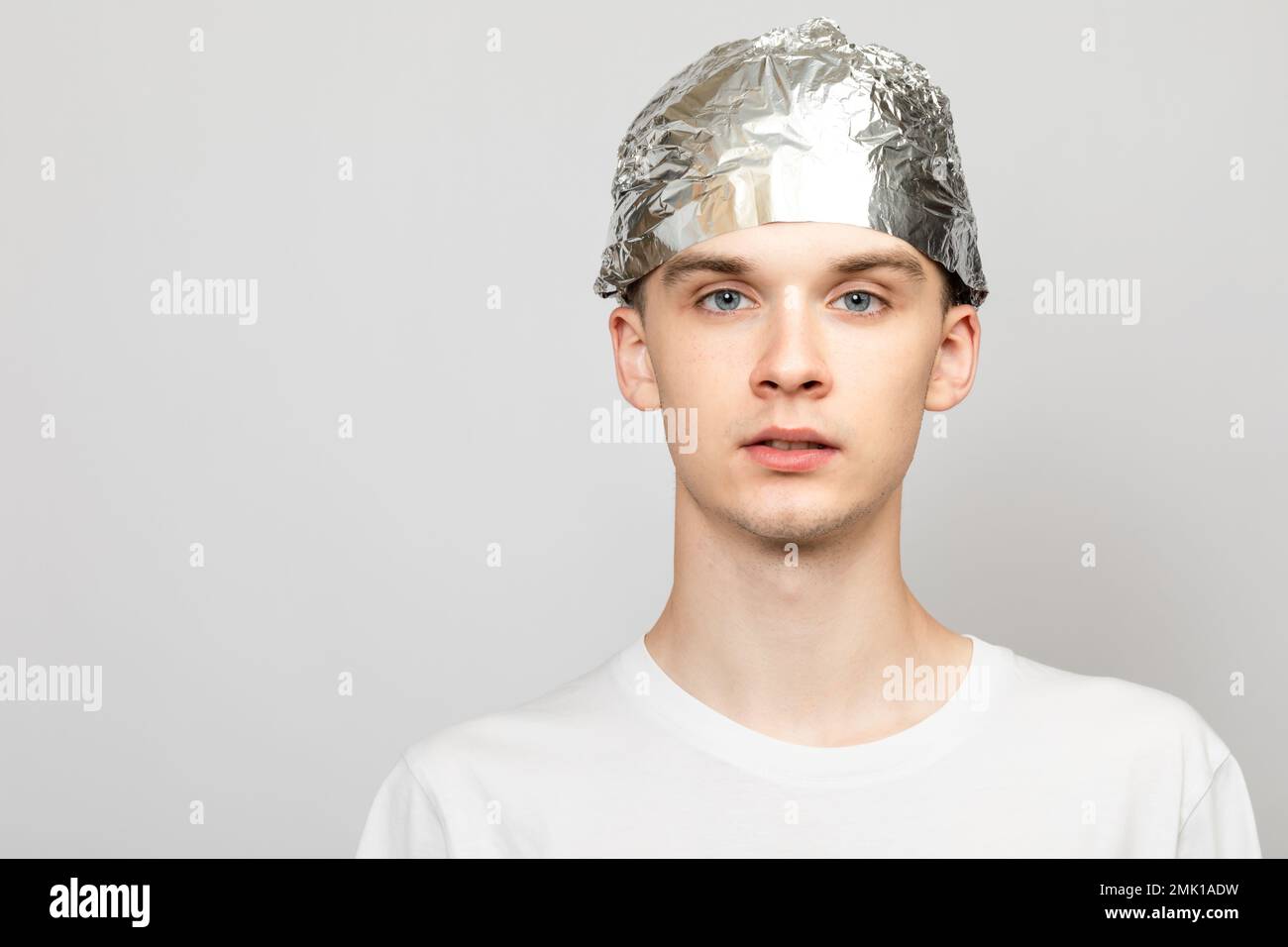 Portrait of young man wearing tin foil hat. Conspiracy theories and paranoya concept. Studio shot on gray background Stock Photo