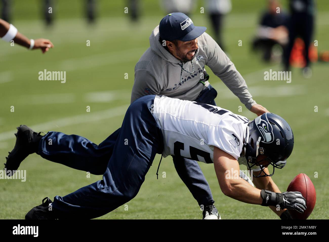 Seattle Seahawks linebacker Cody Barton, bottom, dives for the ball after  it was bobbled by running backs coach Chad Morton, top, during a drill at  NFL football rookie mini camp, Friday, May