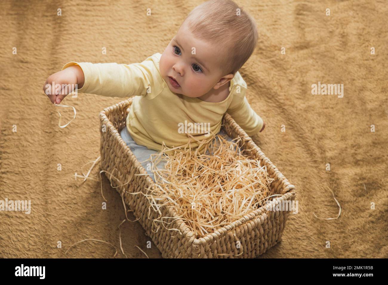 charming Baby sitting in a square wicker basket with straw Stock Photo