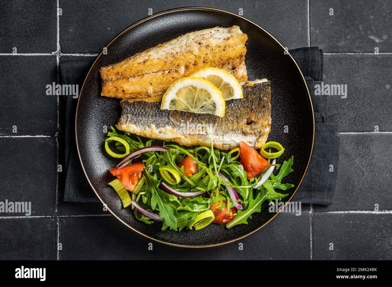 Roasted sea bass fillet with salad, Branzino fish. Black background