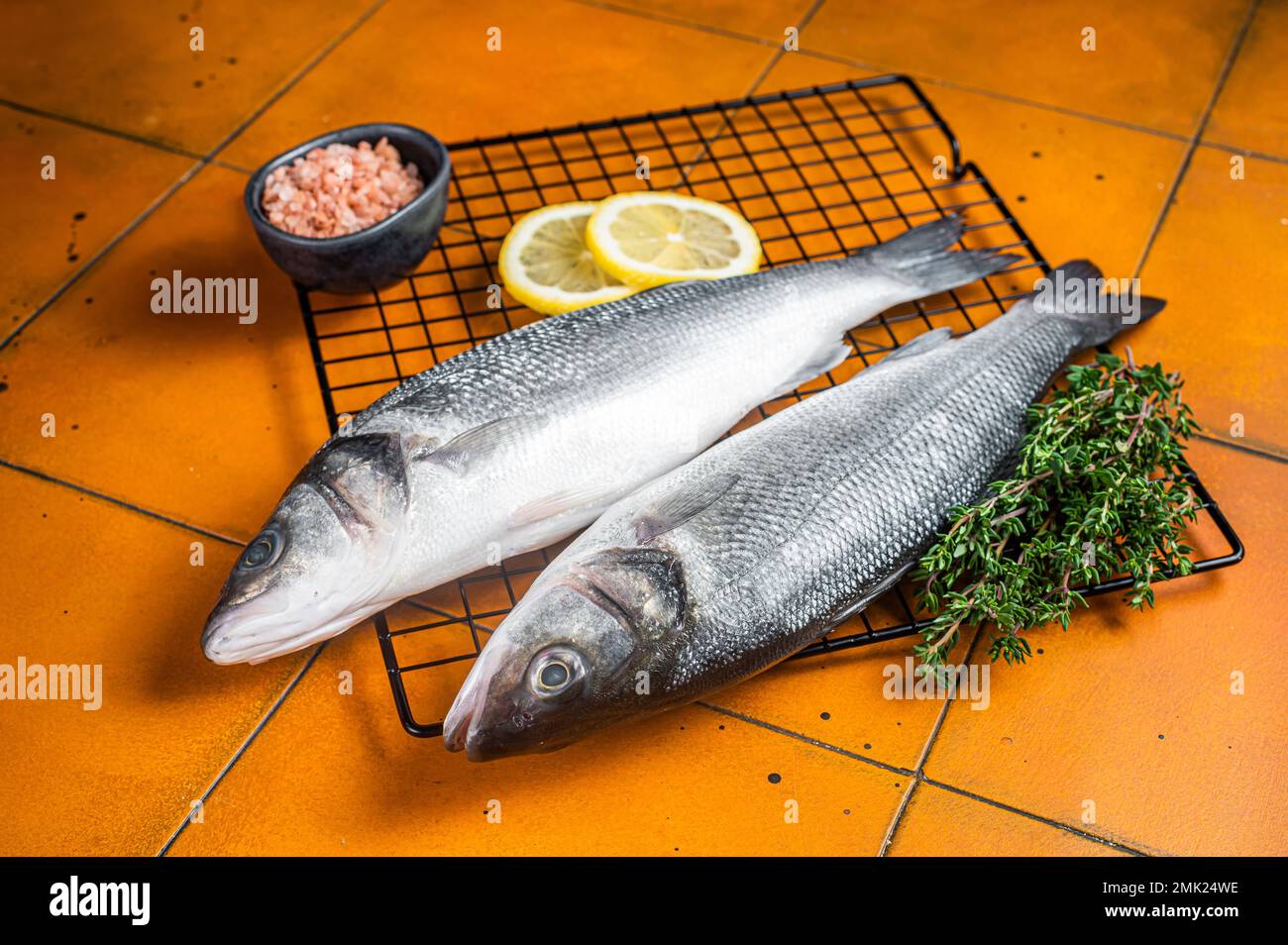 Raw Sea Bass fish with lime and herbs. Orange background. Top view