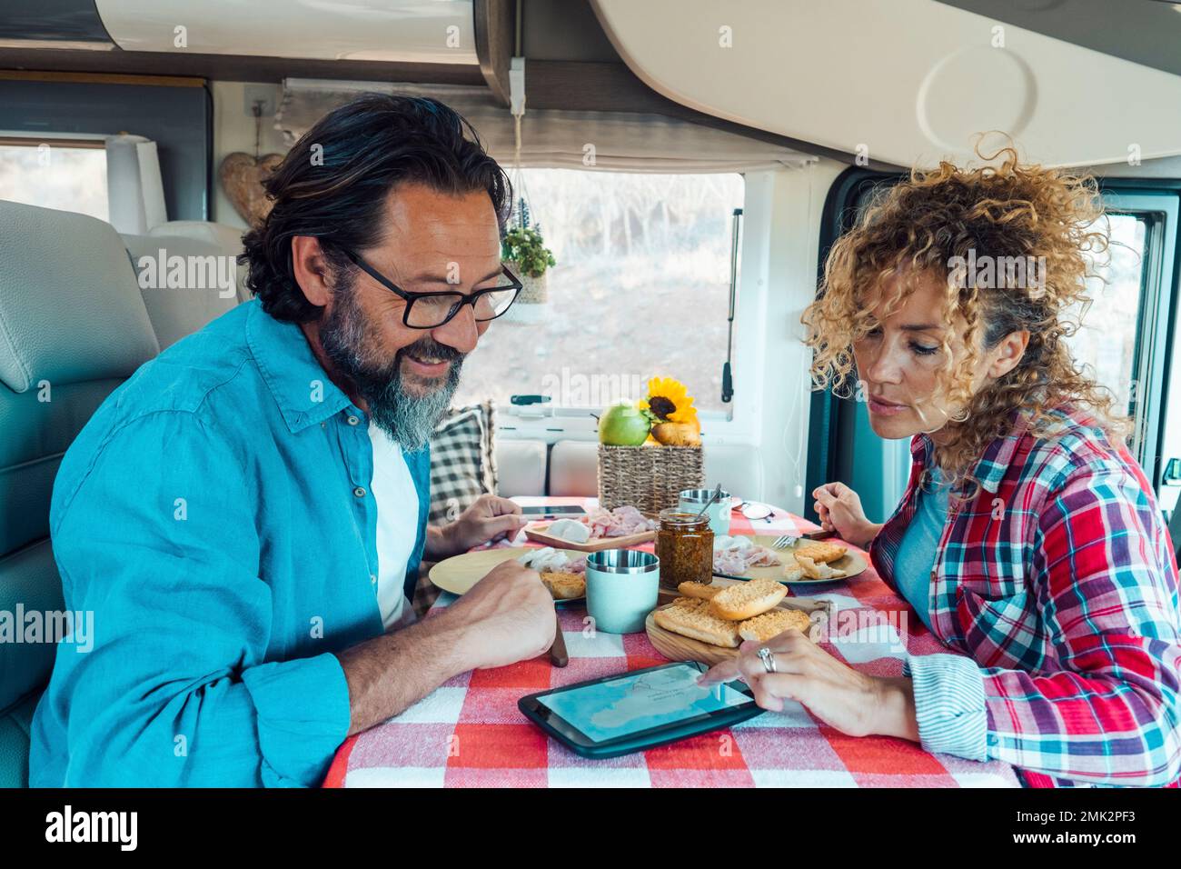 Couple man and woman inside a camper van planning next travel destination together using gps modern device on the table. Lunch time on vehicle motor h Stock Photo