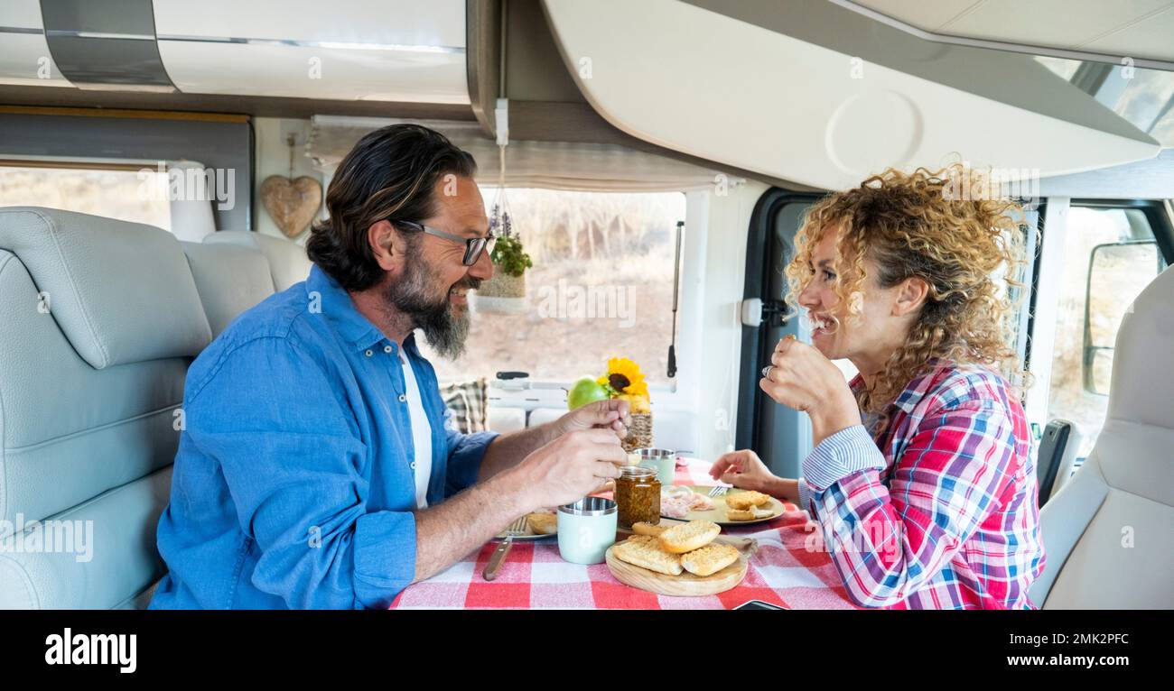 Happy couple spending time together having fun during lunch inside a camper van vehicle in free travel on the road vacation. People with camping car h Stock Photo