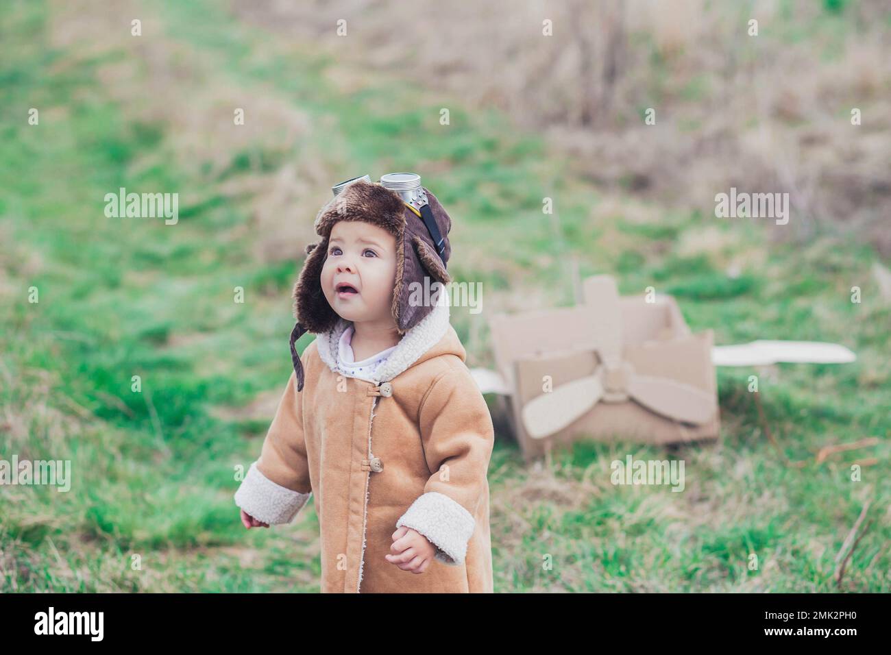 Charming baby in aviator's clothes stands near a cardboard plane  Stock Photo