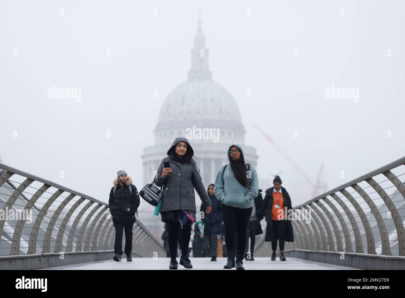 Heavy fog descends London this morning.   Pictured: Commuters brace the cold weather as they cross Millennium Bridge. St Paul’s Cathedral in the back Stock Photo