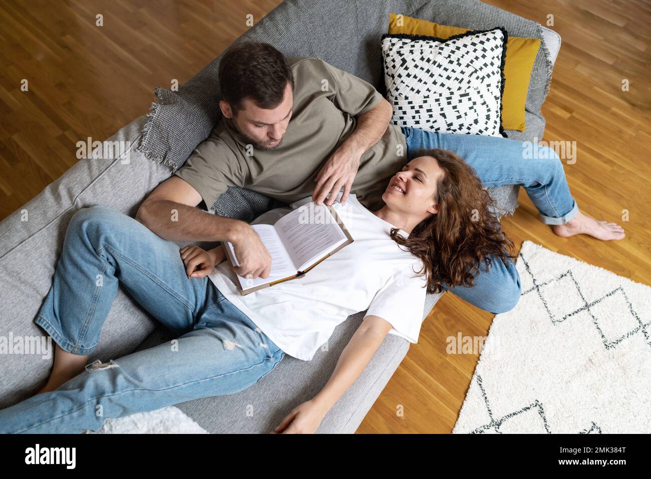 Couple in love lying down on sofa together reading book and smiling. Stock Photo