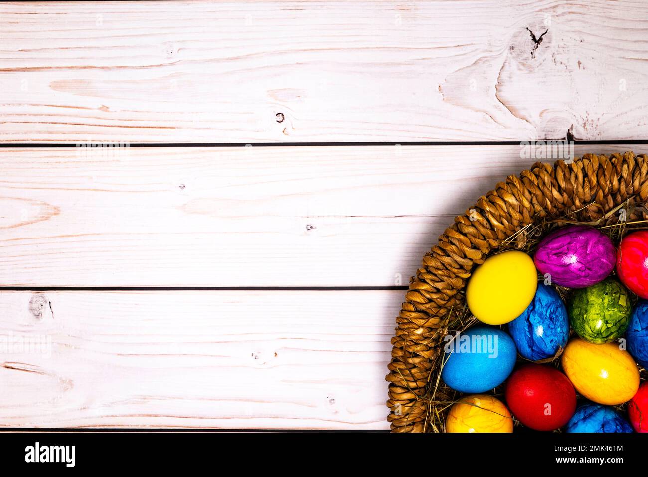 round easter basket with colorful easter eggs on rustic white wooden tabletop Stock Photo