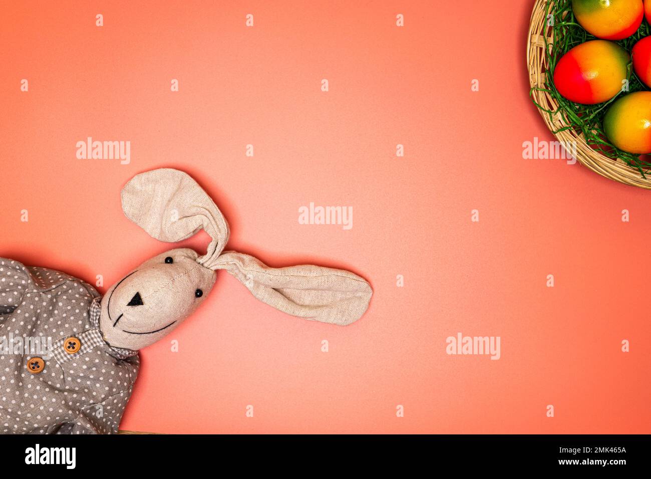 cute fabric easter bunny on orange background with easter basket and multiple colored easter eggs Stock Photo
