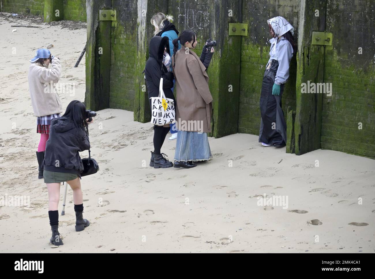 London, England, UK. Young Asian photographers (students?) photographic a model on the south bank of the River Thames at low tide. Stock Photo