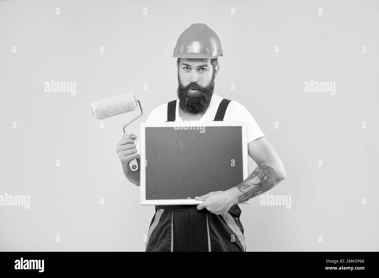 amazed man painter in helmet and work clothes hold paint roller and