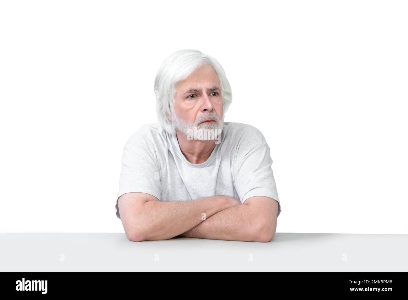 Horizontal shot of an old man sitting at a table with his arms crossed