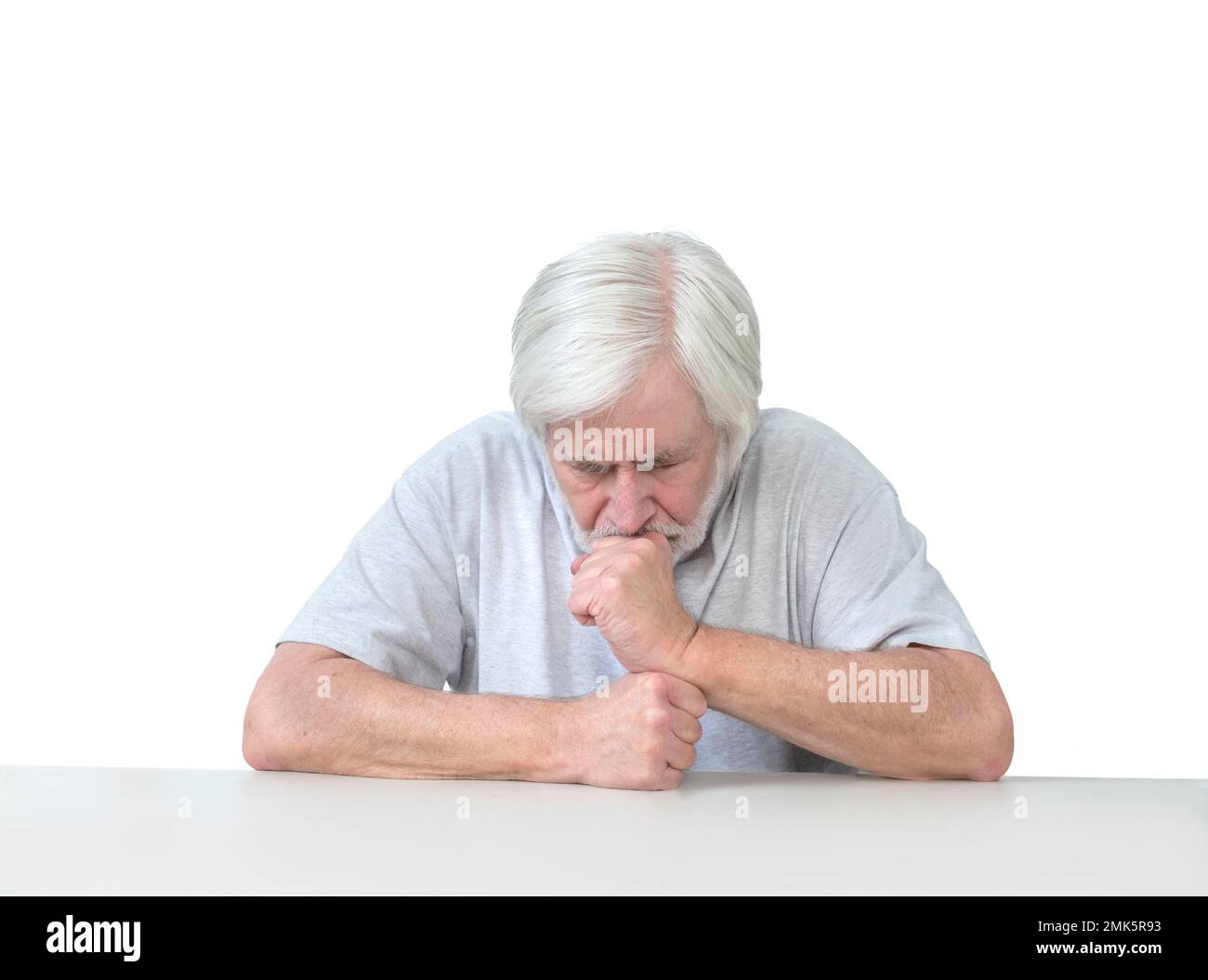 Horizontal shot of a white haired old man sitting at a table leaning his head on his hands in grief, worry or prayer.  Isolated on white.  Lots of cop Stock Photo