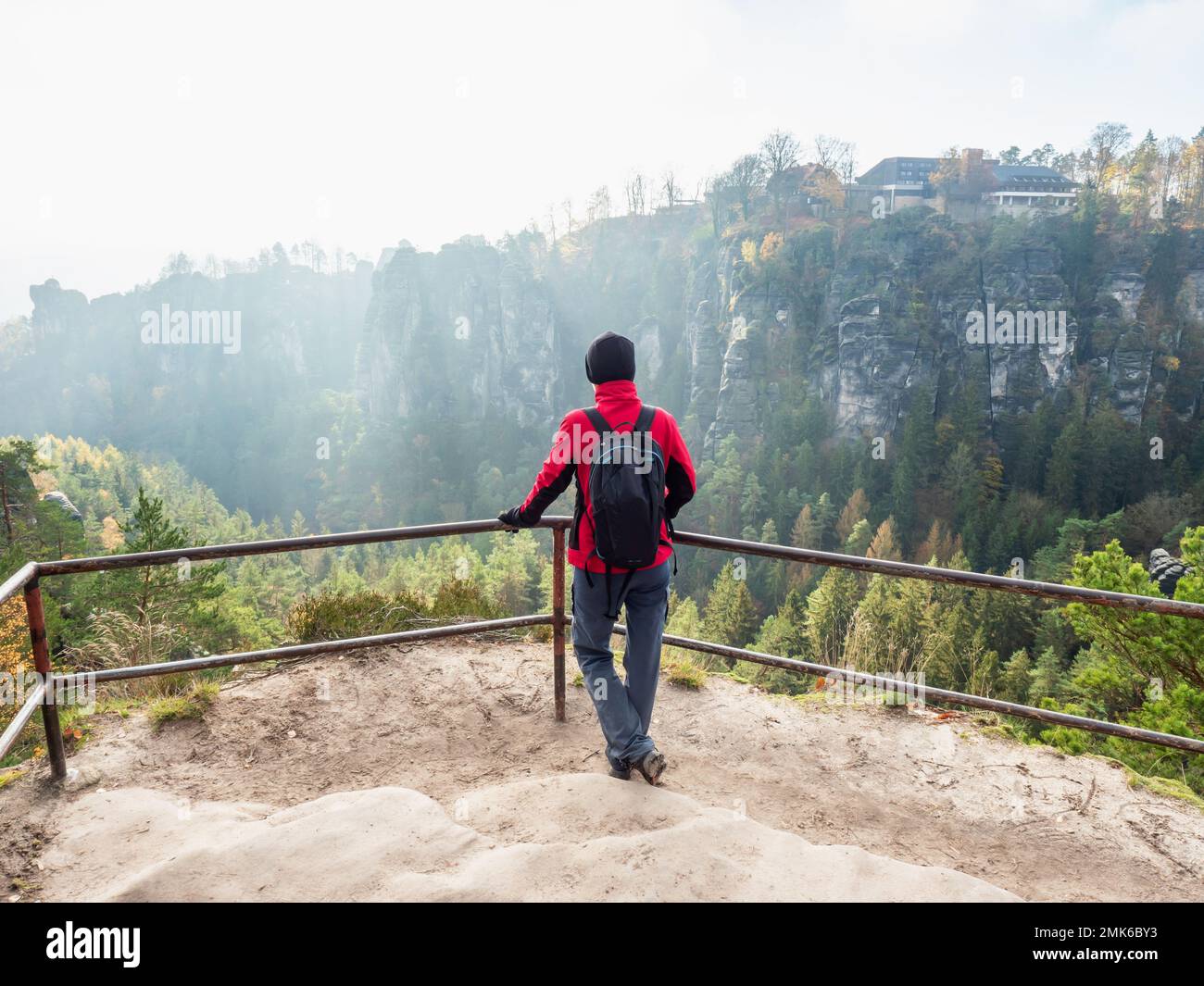 Woman hiker with black backpack is staying on view point and shouting into vally bellow. Happy woman above Bastei Bridge, Saxony park. Stock Photo