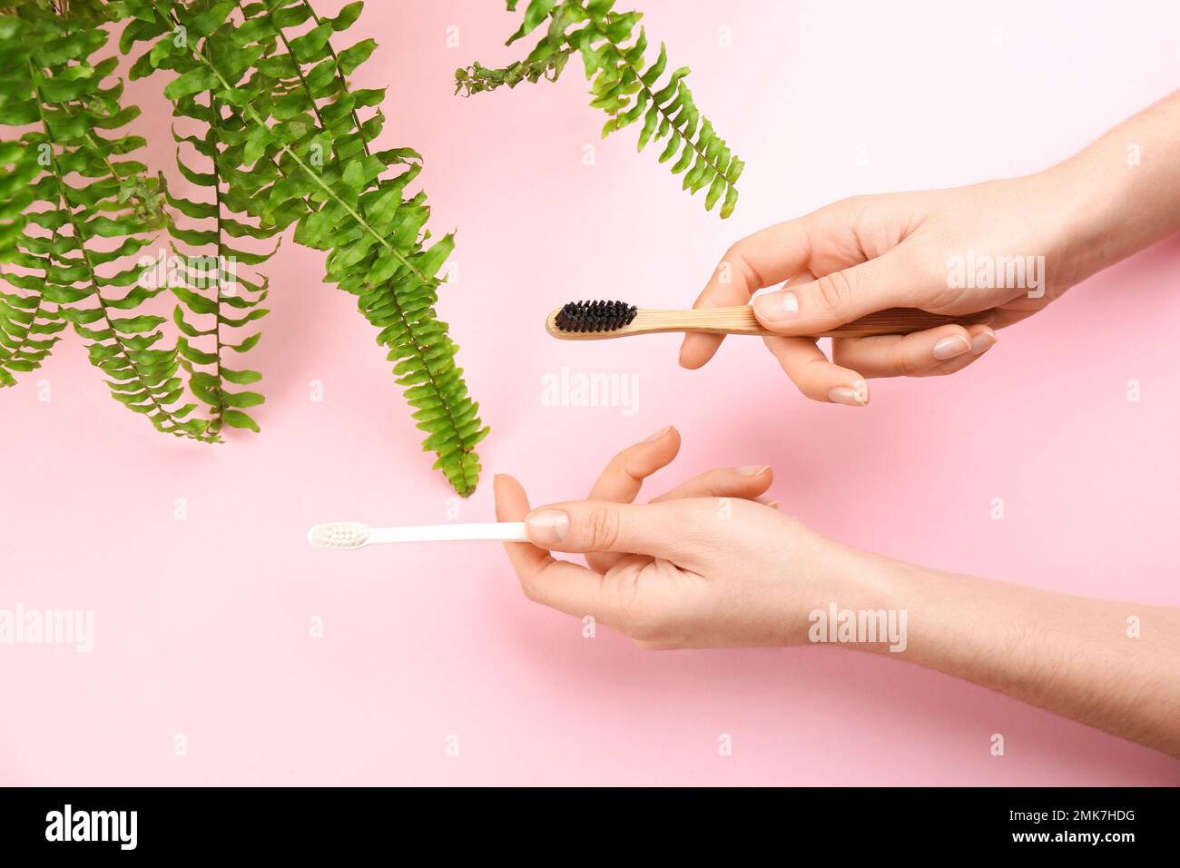 Woman holding natural bamboo and plastic toothbrushes on pink background, top view Stock Photo
