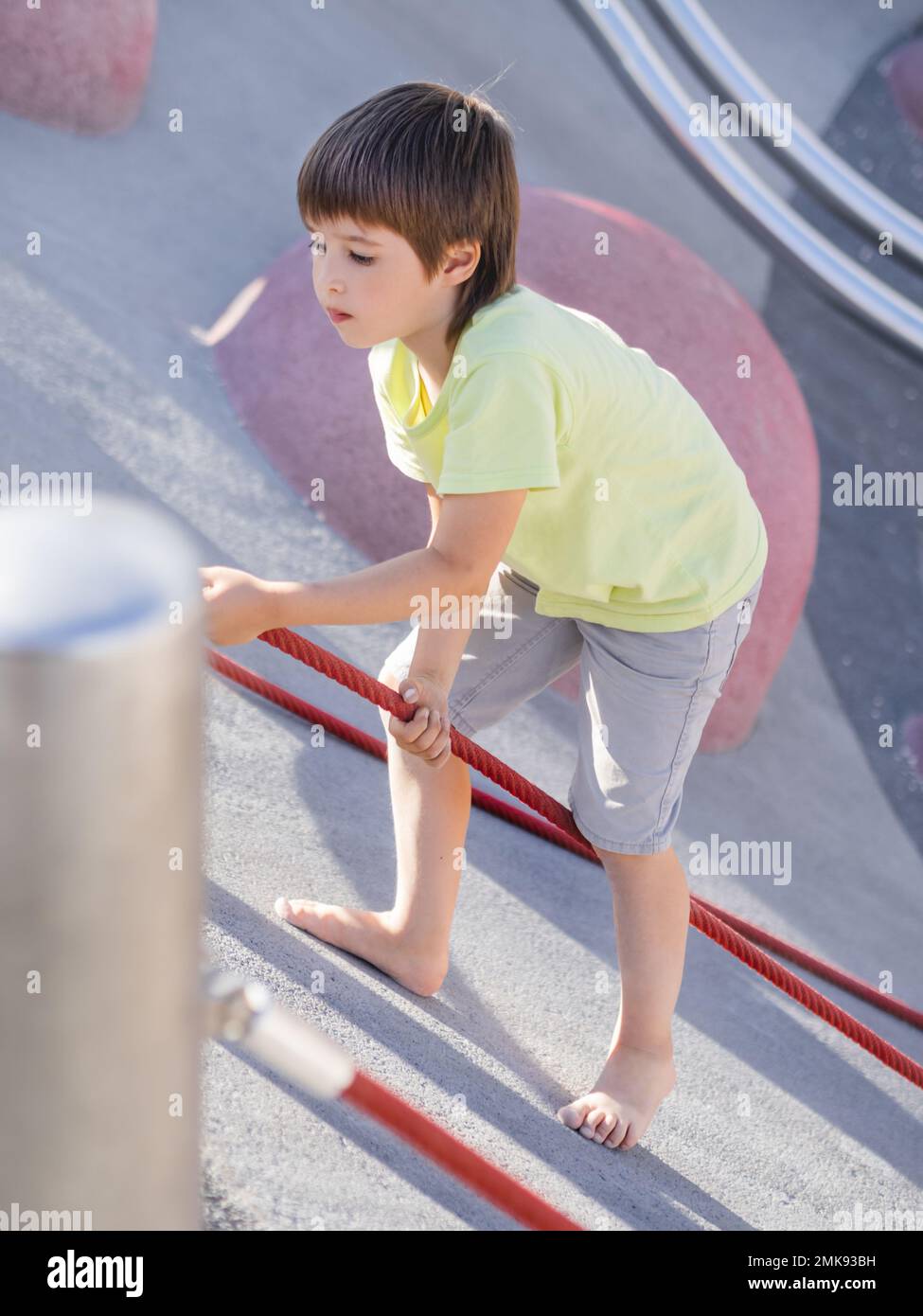 Boy climbes up a concrete slope of modern children's sports and playground. Kid overcomes fear and learn new things. Active leisure outdoors. Sporty l Stock Photo