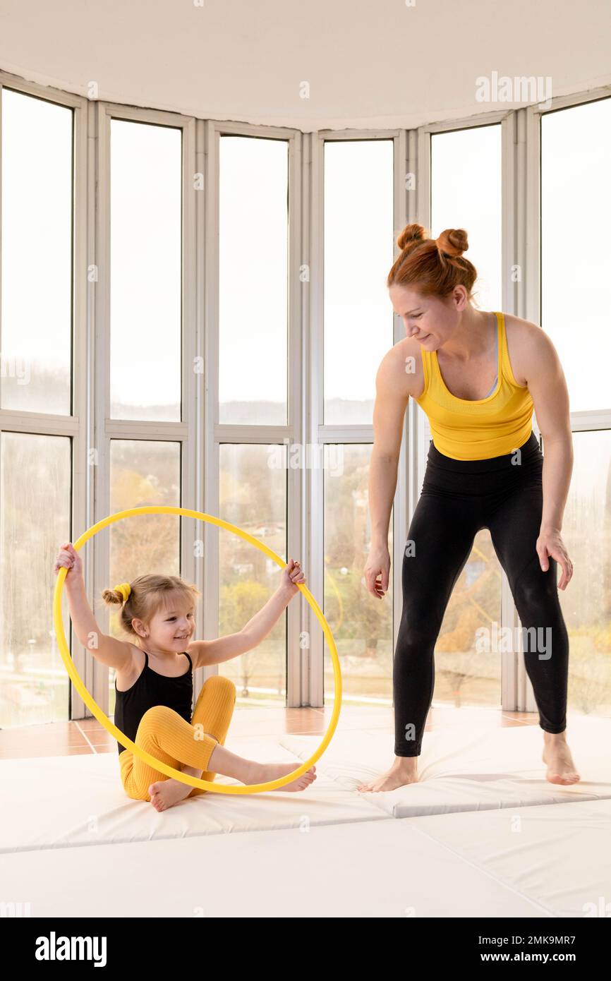Young fit mom and her daughter having fun with hula hoop in a gym Stock Photo