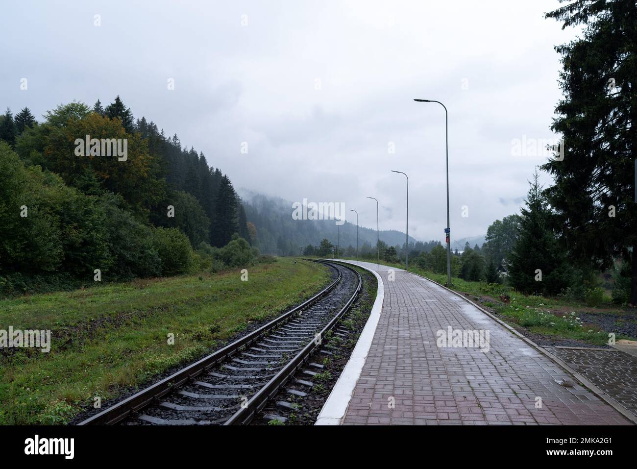 Railway station platform. Railroad leading to the mountains. Cloudy