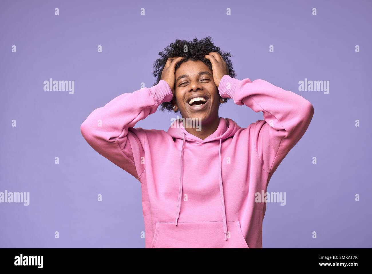 Happy hipster African American teen guy wearing pink hoodie isolated on purple. Stock Photo