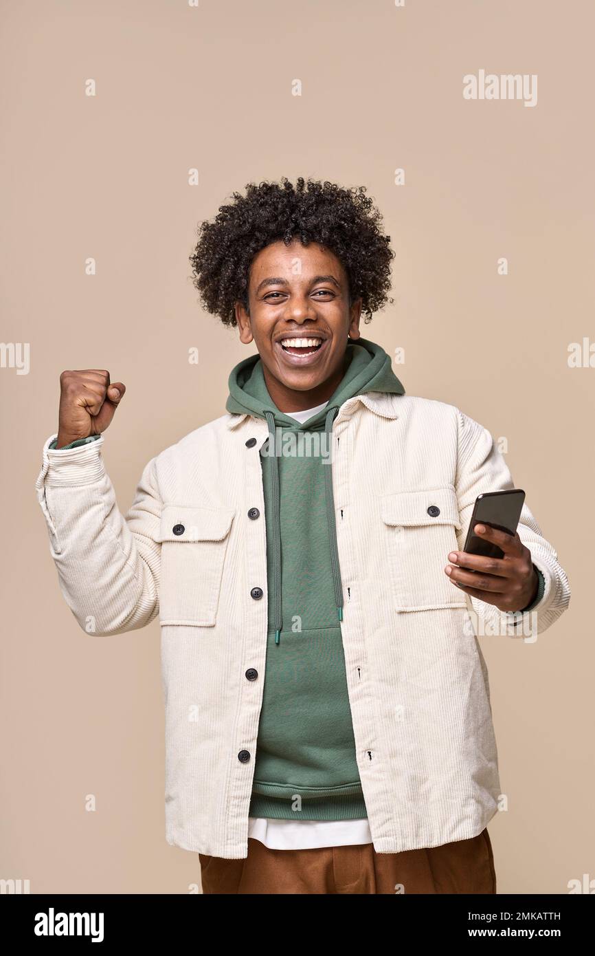Happy African teen winner holding mobile phone winning game online. Stock Photo