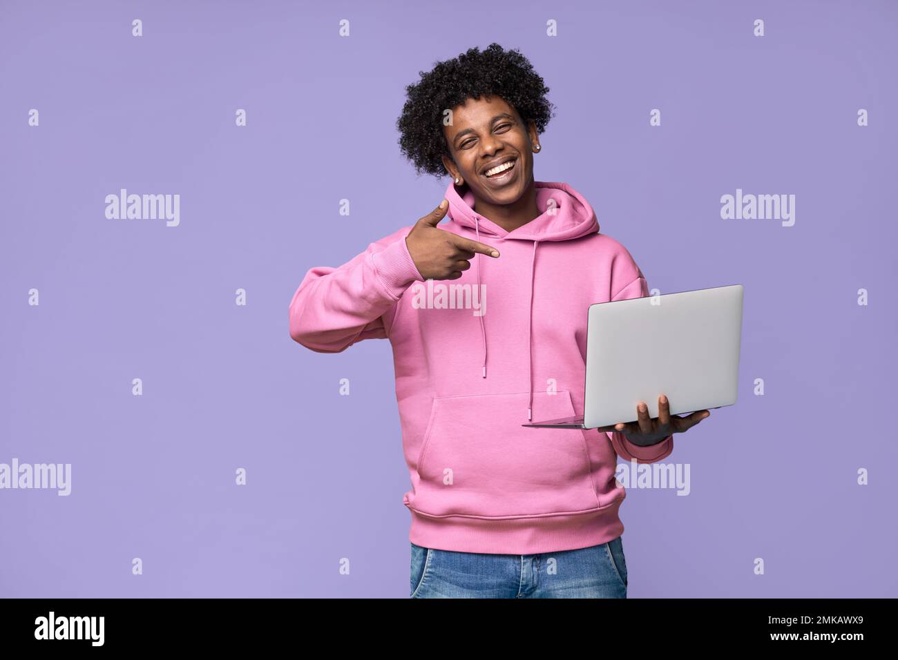 Happy African teen student holding pointing at laptop isolated on purple. Stock Photo