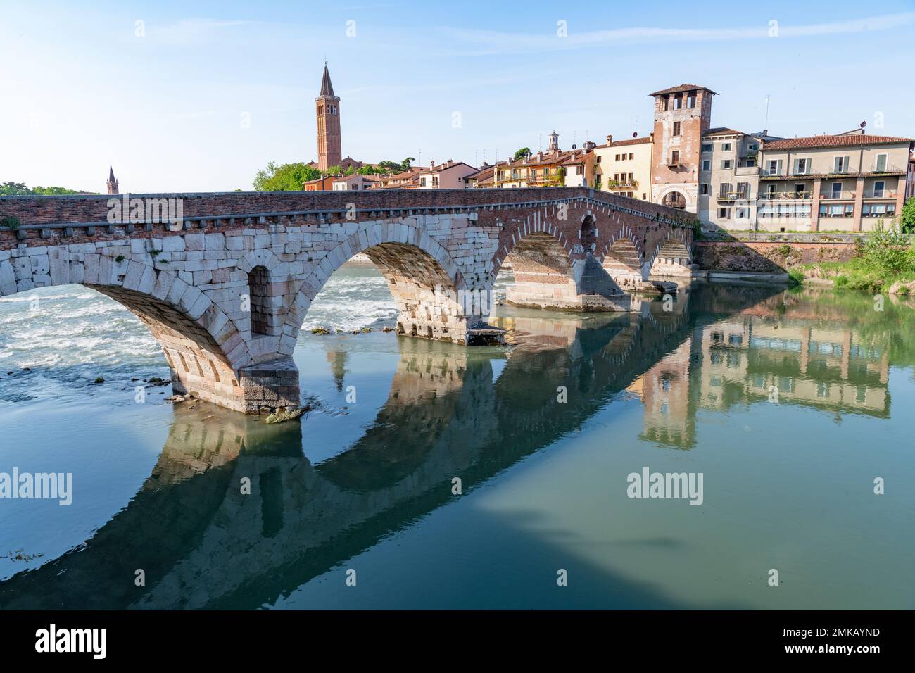 Water flowing under the arches of the Ponte Pietra bridge which spans the Fiume Adige in Verona, Italy set against clear blue skies. The bridge is in Stock Photo