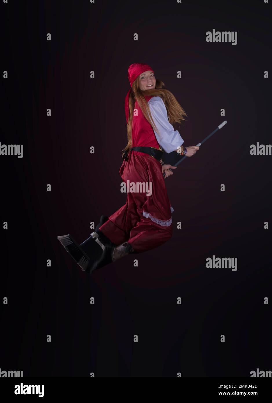 woman with long hair disguised as a pirate in a red suit and with a yellow balloon in the shape of a sword in her hand and on a black background photo Stock Photo