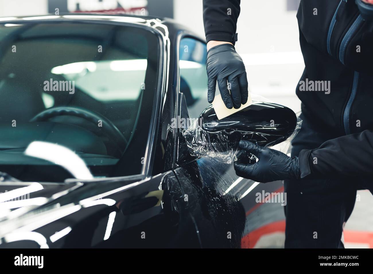 Man wearing black gloves leaning over to smooth out PPF Paint