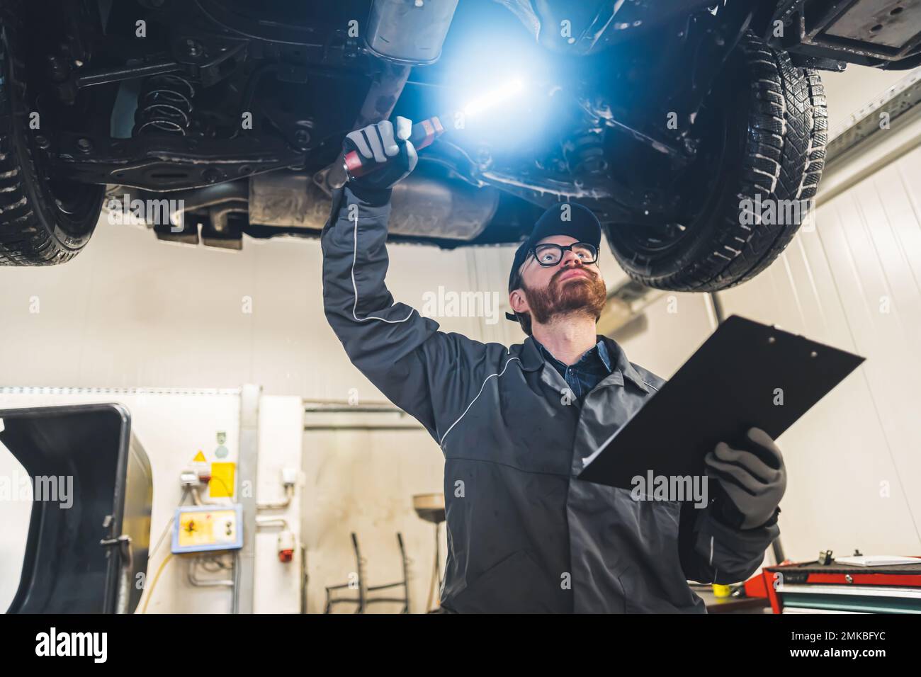Mechanic with a clipboard inspecting the car chassis of a lifted car