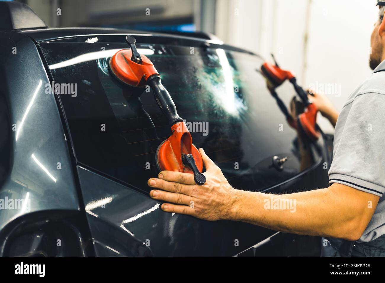 Unrecognisable man instaling rear window pane in the back of car using