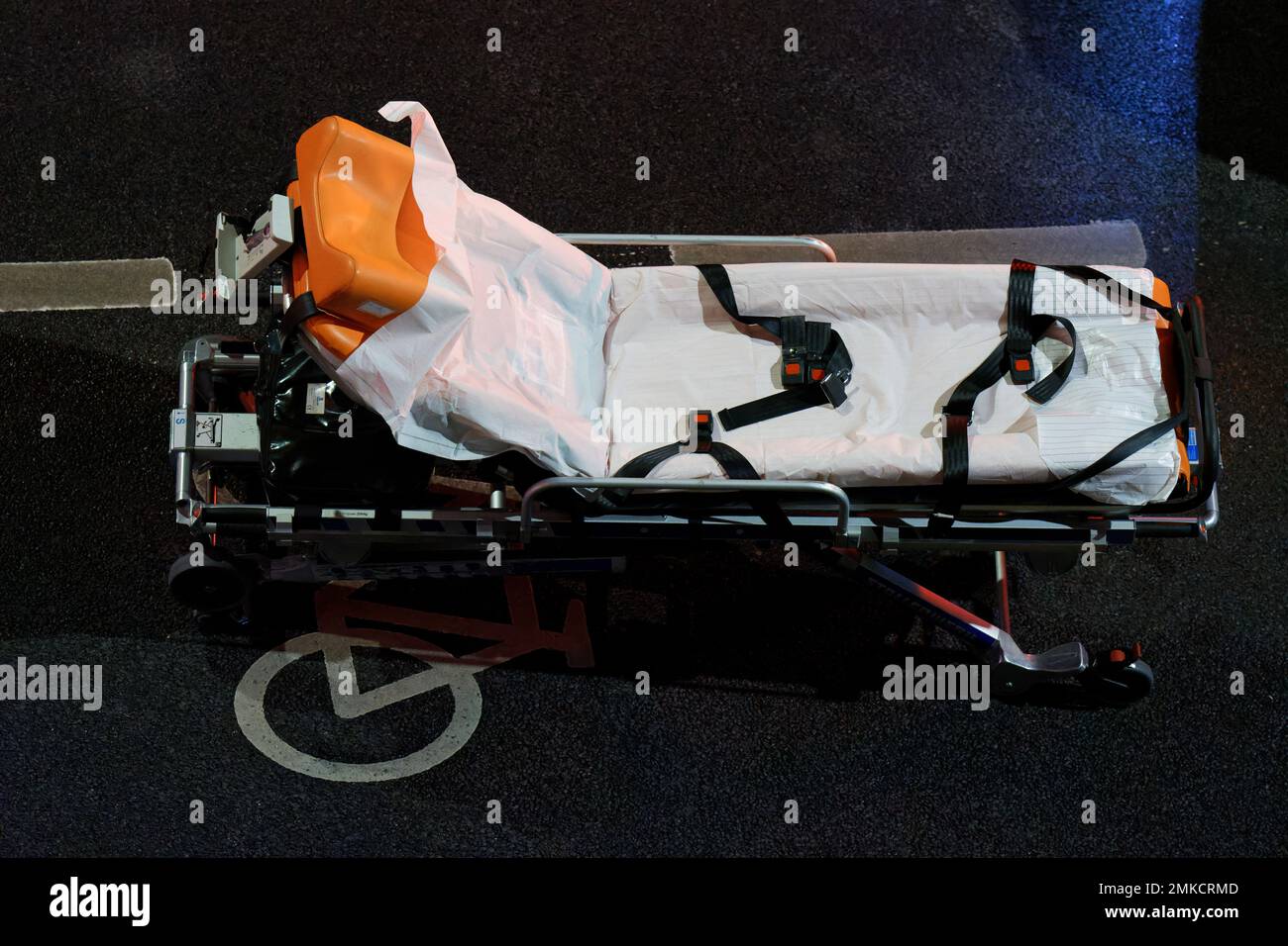 an empty stretcher of an ambulance stands at night on a street with a bicycle lane Stock Photo