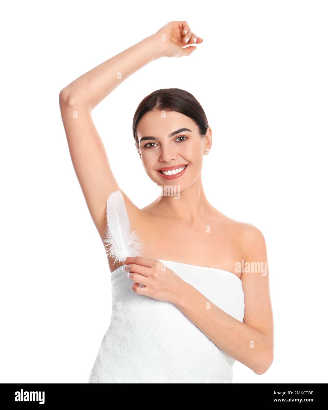 Young woman touching armpit with feather after epilation procedure on white background Stock