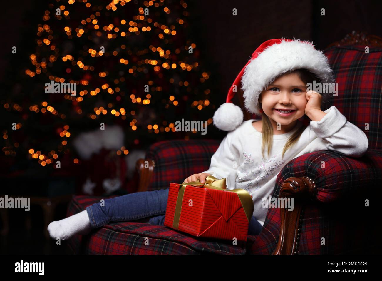 Cute little child with Christmas gift sitting in armchair at home Stock Photo