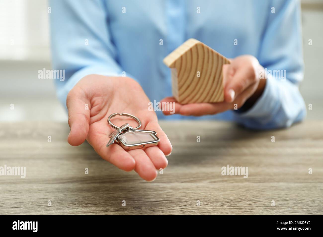 Real estate agent holding house figure and key at wooden table, closeup ...