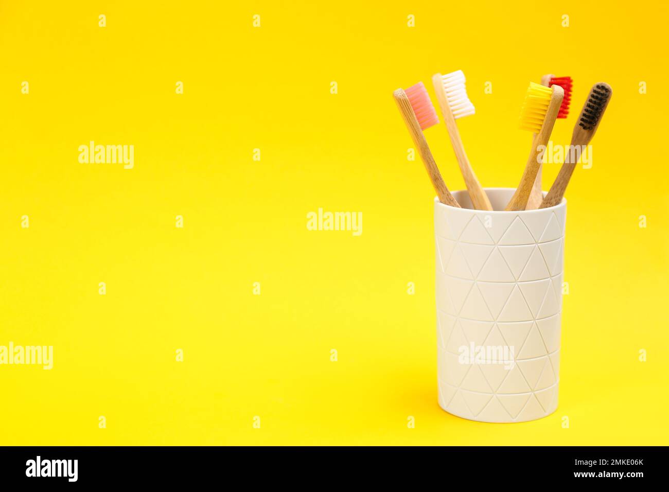 Toothbrushes made of bamboo in holder on yellow background. Space for ...