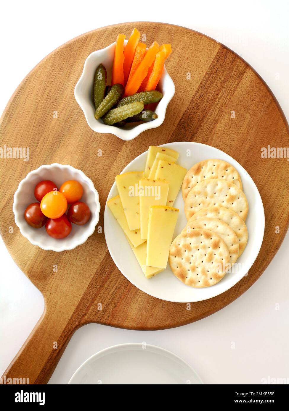 Dutch Gouda cheese slices and water crackers with cherry tomatoes,orange pepper strips and gherkins on round wooden serving board in flat lay composit Stock Photo
