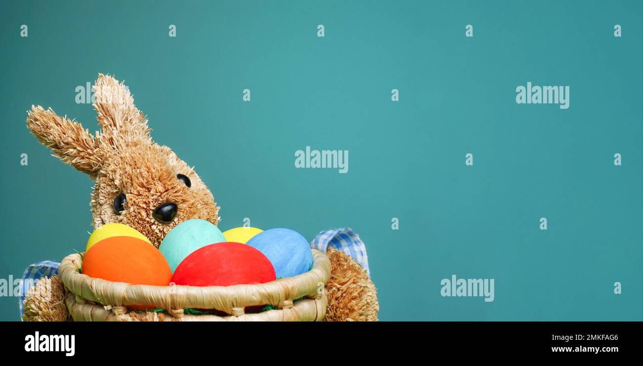 Easter colorful eggs in a straw bunny basket on green blue background ...