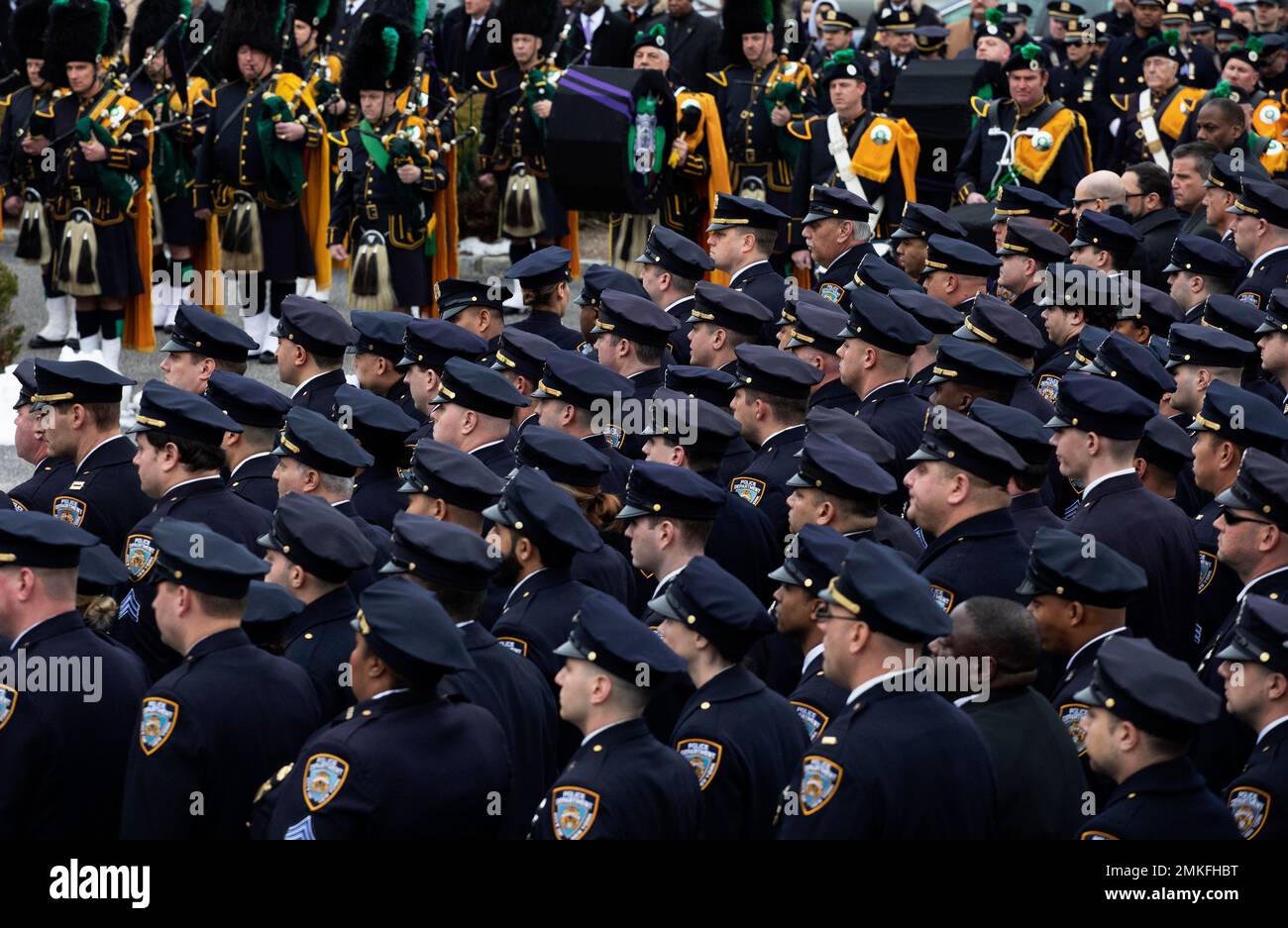 Police officers and a bagpipe band stand at attention during the