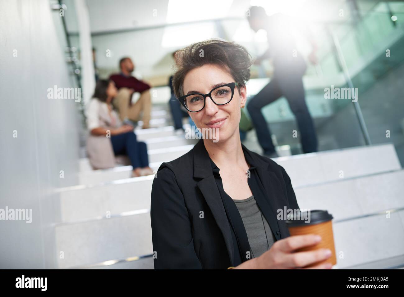 You need the right attitude to succeed. Portrait of a young creative sitting on a staircase in a modern office with colleagues in the background. Stock Photo